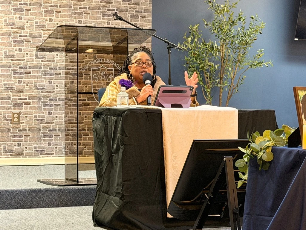 A speaker holding a microphone while seated at a table in the church